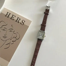 Cargar imagen en el visor de la galería, Vintage-inspired women's quartz watch with brown vegan leather strap and classic dial, styled on a white surface next to artistic print