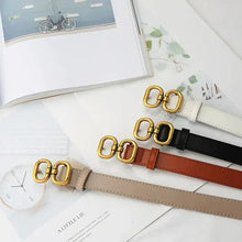 Cargar imagen en el visor de la galería, Elegant leather designer belts for women in various colors with gold buckles, displayed on a table with an open magazine and a clock.