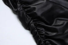 Load image into Gallery viewer, Close-up of black faux leather fabric with ruched detailing, showcasing the sleek texture of the Be So Faux Real Mini Dress.