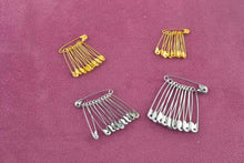 Load image into Gallery viewer, Gold and silver safety pins from eZthings Sewing Accessories Kit on pink background for arts and crafts projects.