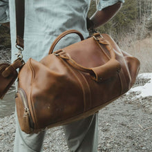 Cargar imagen en el visor de la galería, Traveler with The Dagny Weekender | Large Leather Duffle Bag in rustic outdoor setting.