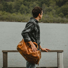 Cargar imagen en el visor de la galería, Man standing by lake with The Dagny Weekender | Large Leather Duffle Bag over shoulder