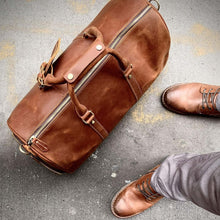 Cargar imagen en el visor de la galería, The Dagny Weekender | Large Leather Duffle Bag with elegant design on concrete surface with stylish brown shoes.
