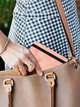 Cargar imagen en el visor de la galería, Woman placing a leather blocking passport holder into a handbag for secure travel with RFID protection.