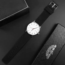 Cargar imagen en el visor de la galería, Elegant black leather quartz watch with a white dial, featuring vegan leather strap, displayed with branded black packaging.