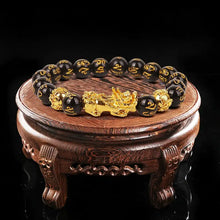 Load image into Gallery viewer, Feng Shui Wealth Bracelet with gold Pixiu charm and black beads, displayed on a wooden stand, symbolizing prosperity and good fortune.