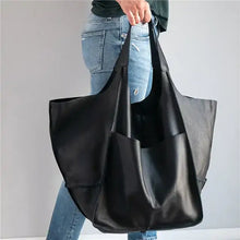 Cargar imagen en el visor de la galería, Person holding a black retro luxury shoulder bag made of vegan PU leather, showcasing its spacious design and casual elegance.