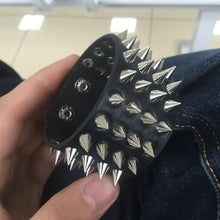 Cargar imagen en el visor de la galería, Faux leather bracelet with spikes showcasing punk-inspired style, held by a hand above a denim background. Ideal for edgy fashion.