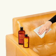 Load image into Gallery viewer, Person using Lint-Free Application Cloth with Leather Honey products on a tan leather couch for smooth, debris-free application.