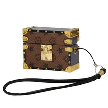 Cargar imagen en el visor de la galería, Brown leather AirPods Pro case with strap and gold accents, resembling a small vintage trunk, elegant and stylish.