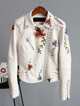 Load image into Gallery viewer, Floral print faux leather jacket with punk rock stud details and romantic embroidery, hanging on a wooden hanger.