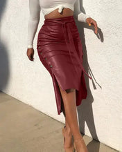 Load image into Gallery viewer, Woman wearing high-waist burgundy faux leather skirt with belt and button trim, showcasing side slit and bodycon fit.
