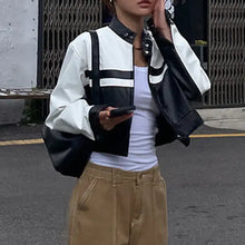 Charger l'image dans la galerie, Woman wearing a stylish patchwork vegan leather jacket with bold black and white design, holding a phone, street scene background.