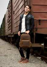 Load image into Gallery viewer, Man standing beside train holding The Langley Backpack | Genuine Vintage Leather Backpack, stylish travel accessory for daily use.