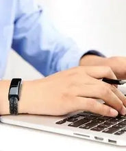 Cargar imagen en el visor de la galería, Person wearing a USB leather charging braided bracelet while typing on a laptop, showcasing style and functionality.