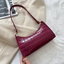 Cargar imagen en el visor de la galería, Vegan leather shoulder bag in burgundy, crocodile pattern, placed on a beige fabric background.