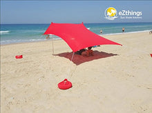 Charger l'image dans la galerie, eZthings UV Sun Shade Beach Shelter in red, providing sun protection on a sandy beach with visible sandbag anchors.
