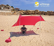 Charger l'image dans la galerie, Person sitting under red beach shade canopy with sandbag anchors, designed by eZthings, on a sunny beach. Provides UV protection.