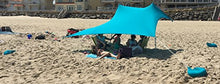 Charger l'image dans la galerie, Beachgoers enjoying shade under a bright blue eZthings UV sunshade with sandbag anchors.