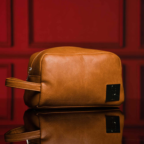 Brown leather toiletry bag with a sleek design, perfect for travel and organization, set against a rich red backdrop.