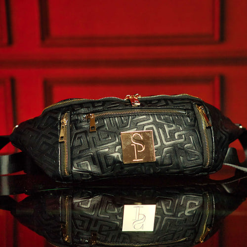 Black Monogram Leather Crossbody Bag with gold accents on a red background.