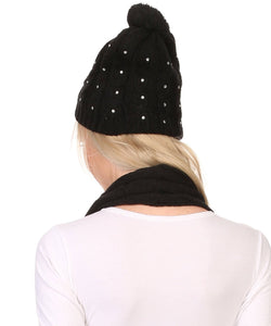 Back view of model wearing black jewel studded cable knit beanie hat with pom pom and matching scarf set.