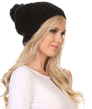 Charger l&#39;image dans la galerie, Unisex cable knit beanie with large pom pom in black, worn by person with long blonde hair, showcasing slouchy fit and modern style.
