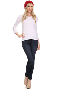 Woman wearing red knit beanie, white top, and dark jeans, modeling winter fashion.