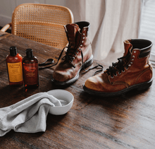 Cargar imagen en el visor de la galería, Leather Cleaner with boots on wooden table, showcasing gentle, non-toxic formula effective on leather, vinyl, and faux leather surfaces.
